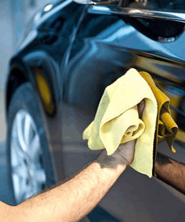 A detailer wiping a black car's body with a cloth after applying Ceramic Coating